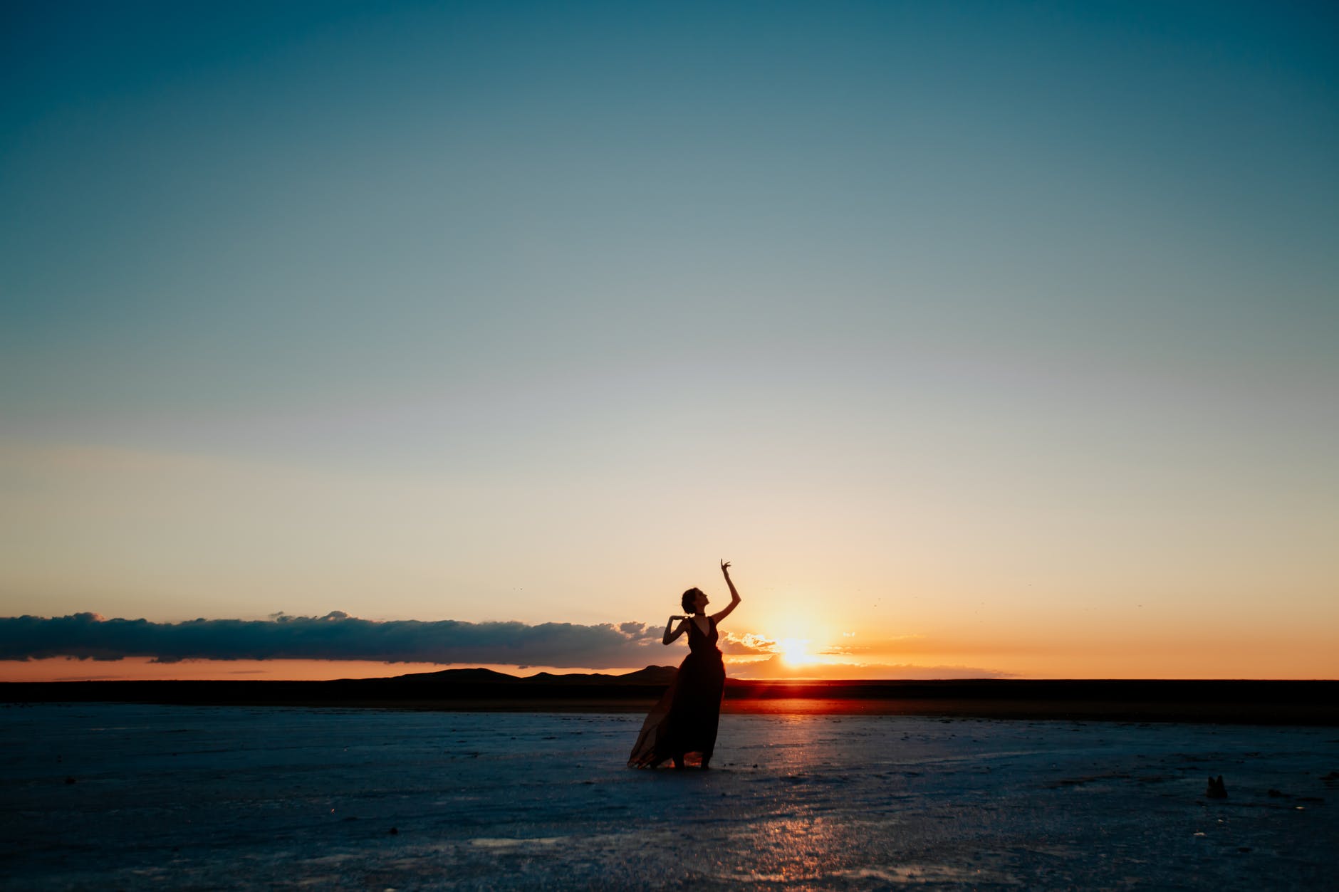 anonymous lady dancing on sandy seashore at sundown